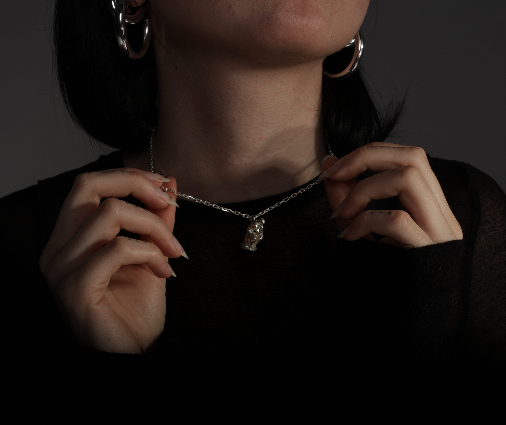 Sterling 925 silver pendant modeled after Rodin's sculpture 'The Thinker,' hanging from a delicate silver chain around the neck of the wearer. The pendant, depicting a seated figure deep in thought, is clearly visible against the dark background, with the person's hands gently holding the chain.