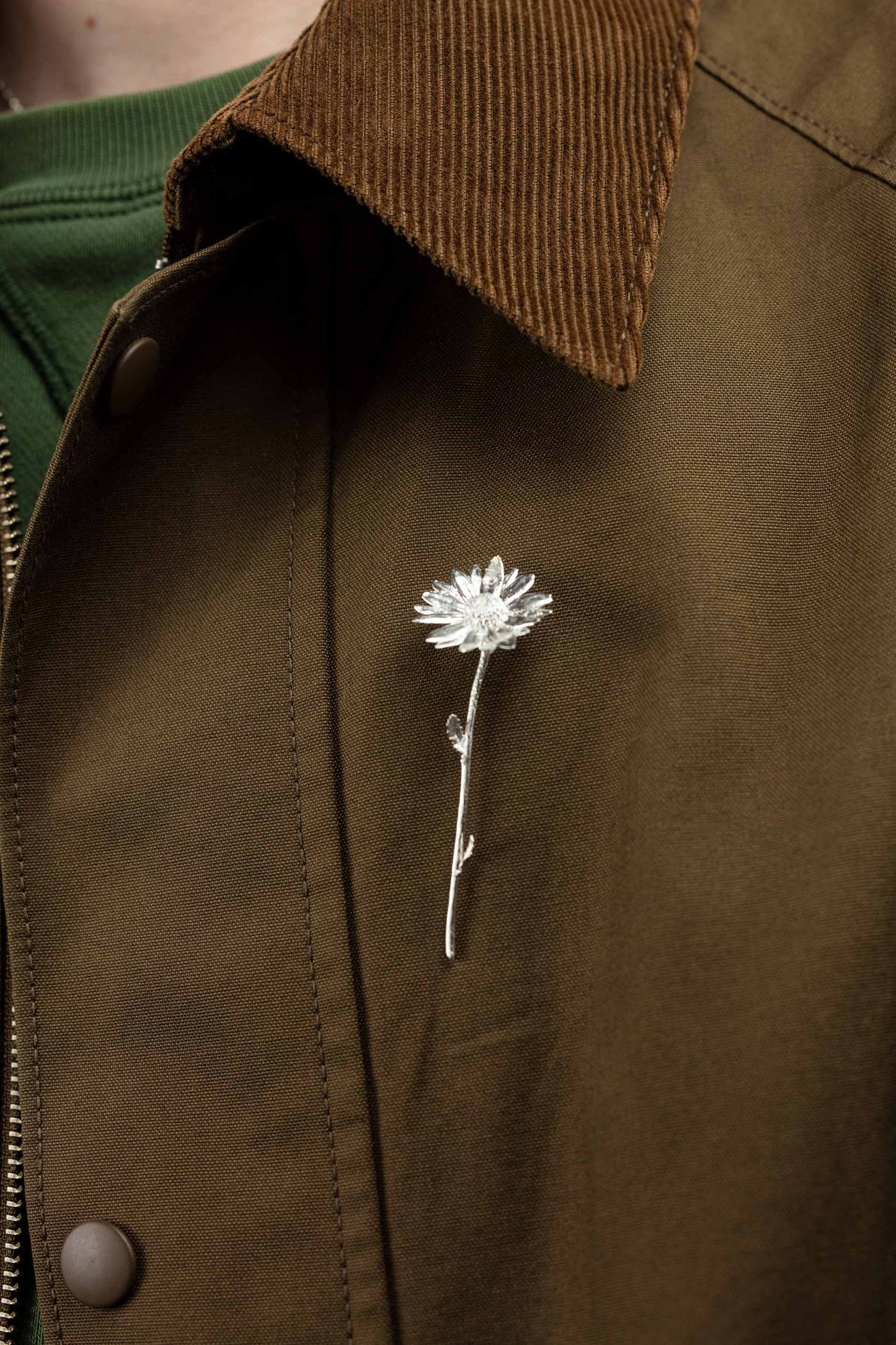 Sterling 925 silver daisy brooch pinned on a brown jacket, showcasing the intricate floral design. The close-up image highlights the delicate details of the silver brooch, with the subtle texture of the jacket fabric serving as a rich backdrop.