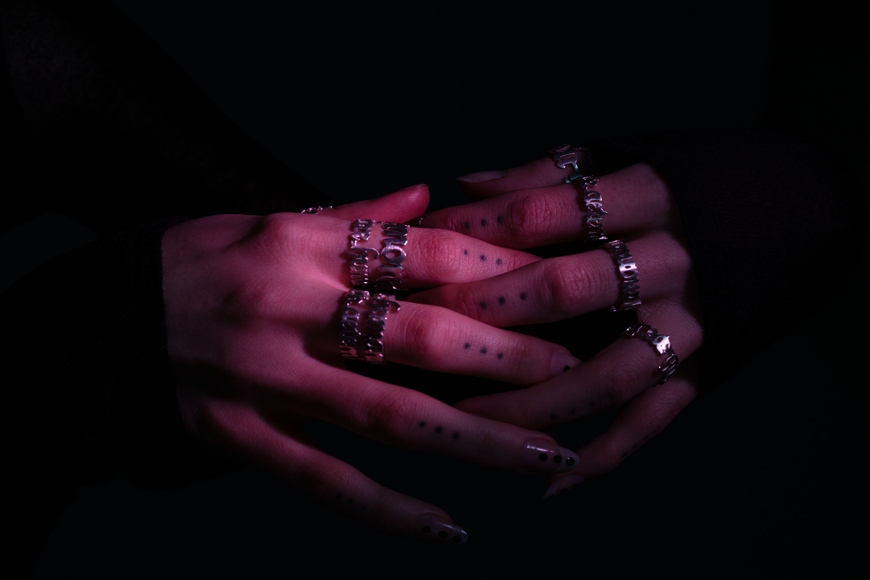 Sterling 925 silver rings, engraved with 'more is more,' 'less is more,' 'sub specie aeternitatis,' and 'errare humanum est,' worn on fingers with dotted tattoos and stylish nails, set against a dark background illuminated with purple and violet lighting, highlighting the intricate shape and modern aesthetic of the rings.