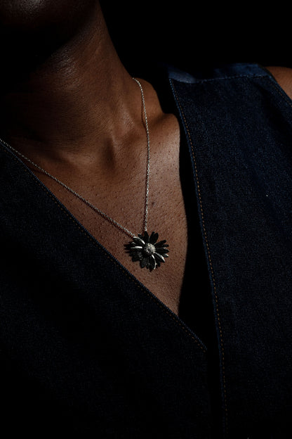 Sterling 925 silver daisy pendant hanging from a chain, worn on the neck of a person dressed in a dark denim top.