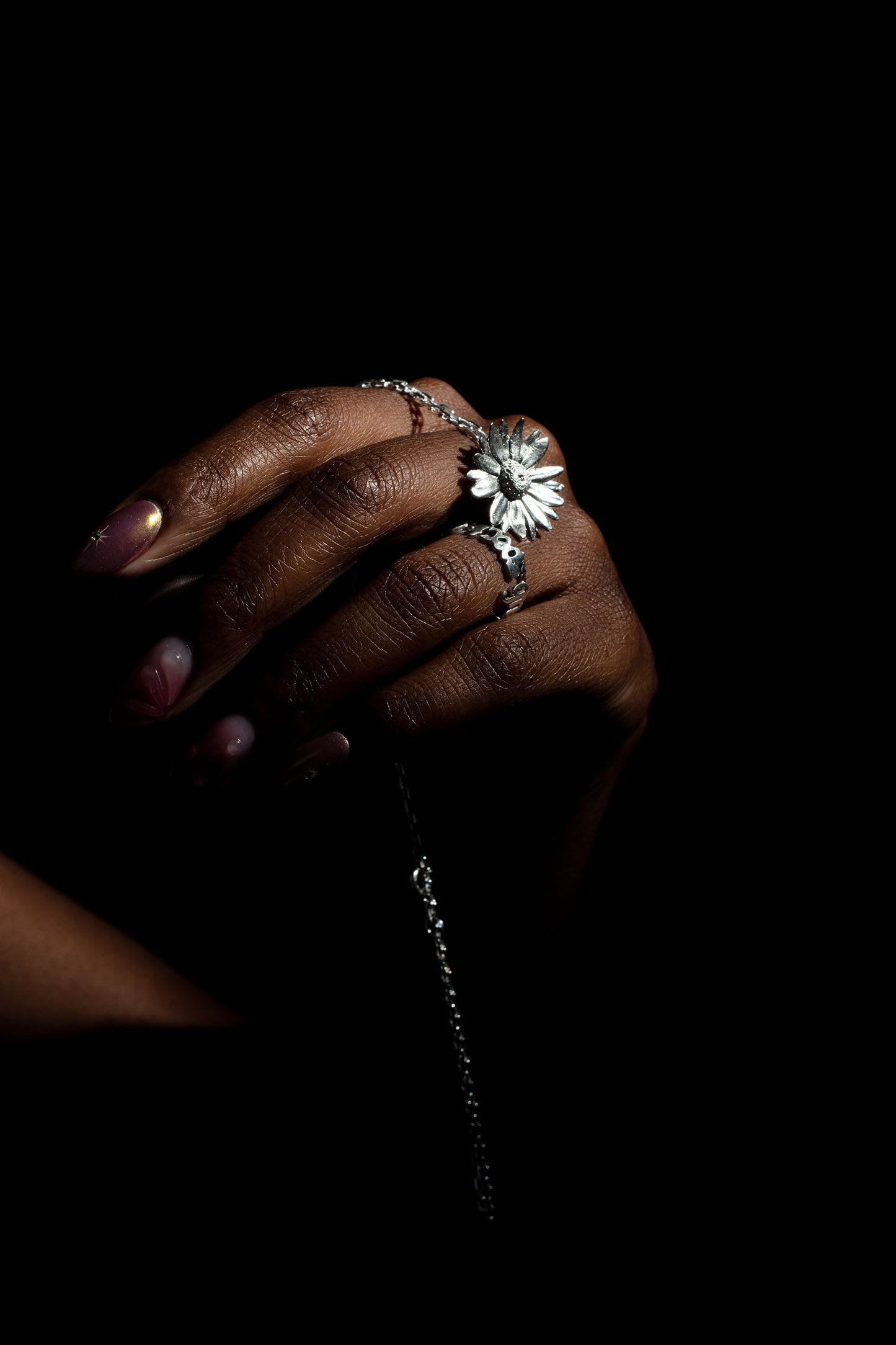 Sterling 925 silver daisy pendant and ring engraved with 'sub specie aeternitatis,' worn on a hand with elegant nails, set against a dark background.